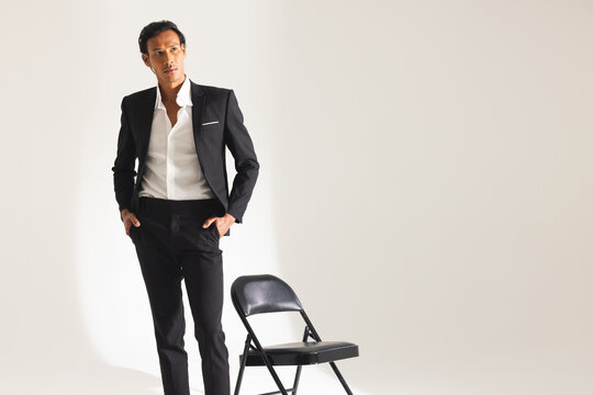 Confident man in stylish suit posing next to chair in fashion studio