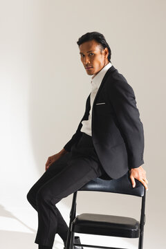 Confident man in black suit sitting on chair, looking at camera