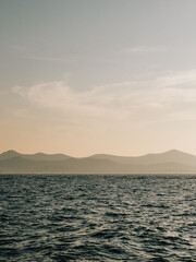Mediterranean sea gently rippling under vibrant sunset, with majestic mountains rising in background, creating tranquil and serene atmosphere perfect for relaxation. Mediterranean sea at sunset
