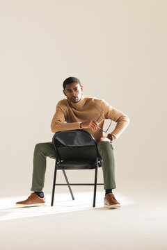 African American man in stylish outfit sitting confidently on chair in studio