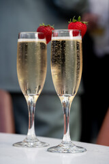 Two champagne flutes with strawberries on rim, filled with bubbly.