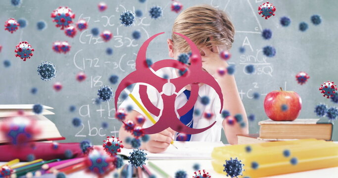Image of Covid 19 coronavirus cells spreading with biohazard symbols over schoolboy writing in schoo
