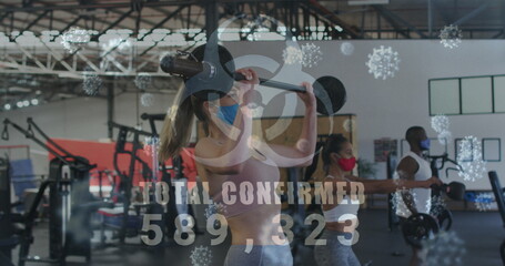 Image of covid-19 cells floating over diverse group wearing face masks working out