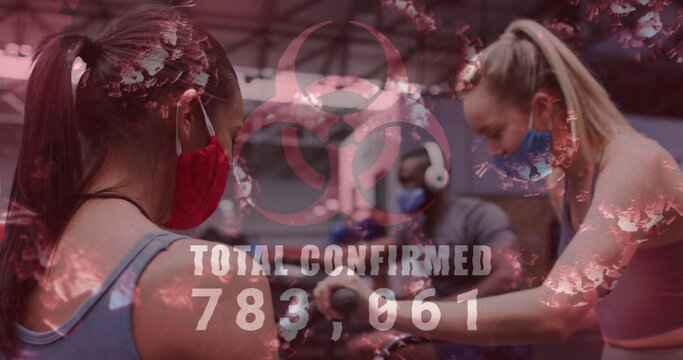 Image of covid-19 cells floating over diverse group wearing face masks working out