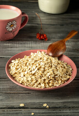 A bowl filled with rolled oats sits on a rustic wooden table, accompanied by a wooden spoon. Nearby, a cup of milk adds to the breakfast vibe, enhancing a calm morning atmosphere