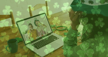 Clover leaves falling against woman wearing shamrock glasses while having a image call at home