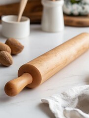 Wooden rolling pin on a white marble countertop. the rolling pin is made of light-colored wood and has a smooth surface. it is resting on a small white bowl with a wooden spoon in it.