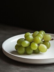 Bunch of green grapes on a white plate. the grapes are round and plump, with a glossy texture. they are arranged in a cluster on the plate, with some overlapping each other.