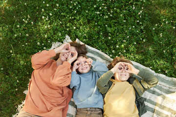 Top view of mother and two boys lying on picnic blanket together and making silly faces looking up...