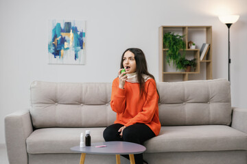 Obraz premium Young girl spraying medicine in mouth,disinfection in her oral, prevention of respiratory infection or Coronavirus COVID-19, protect against the bacteria in throat before the germ enters the lungs