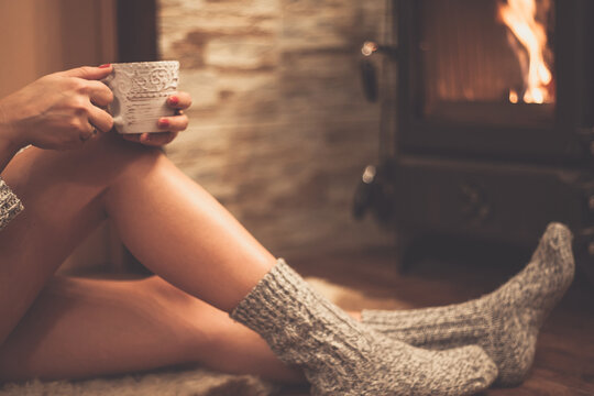 Close-up side view of a woman wearing woolly socks sitting  in front of a wood burning stove with a mug of tea