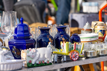 A colorful array of ceramics and glassware on display at a flea market. The collection includes navy blue vases, decorative animal figurines, and various kitchenware, creating a colorful and eclectic 