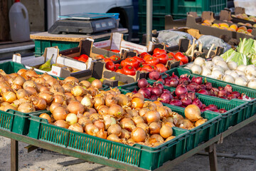 market stall with fresh vegetables including onions, garlic, tomatoes and red onions