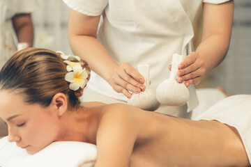 Hot herbal ball spa massage body treatment, masseur gently compresses herb bag on woman body....