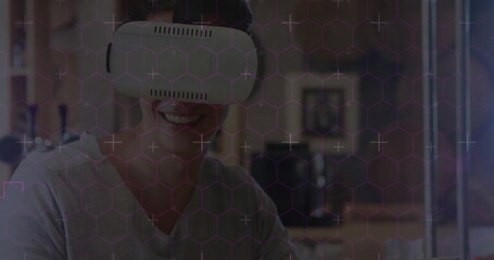 Hexagonal shapes and data processing against caucasian man wearing vr headset using digital tablet