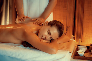 Caucasian woman customer enjoying relaxing anti-stress spa massage and pampering with beauty skin recreation leisure in warm candle lighting ambient salon spa at luxury resort or hotel. Quiescent