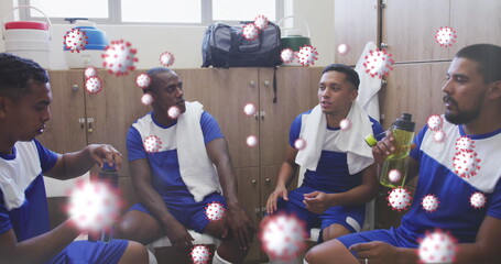 Covid-19 cells floating against team of male soccer players discussing together in locker room