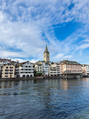 Historic Zurich Waterfront with St. Peter Church Tower and Limmat River.Zurich Cityscape: Medieval Architecture along Limmat River under Blue Sky.