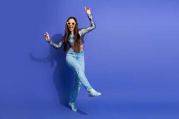Joyful young woman in trendy casual outfit dancing against purple background expressing confidence...