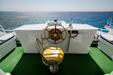 Luxurious yacht helm with vibrant green flooring and golden-brown seating. Overlooks expansive, sparkling Red Sea under clear blue sky. Sunlight reflects on waters surface