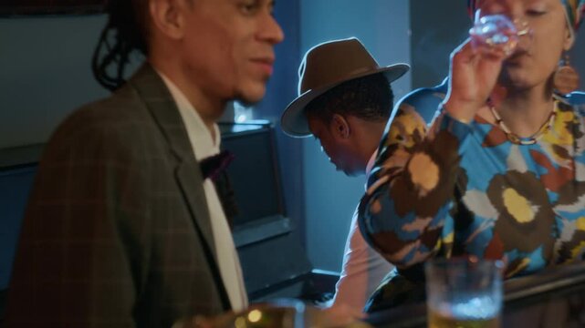 Elegant Biracial woman smoking and sipping wine while listening to man at bar as pianist in background playing soulfully in retro-inspired setting