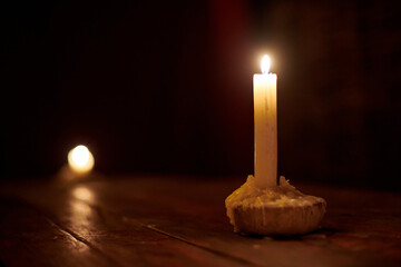 Single candle burns brightly on rustic wooden table in dimly lit room, creating warm, serene...