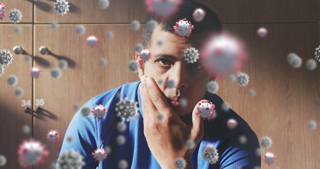 Multiple covid-19 cells floating against portrait of male soccer player sitting in changing room