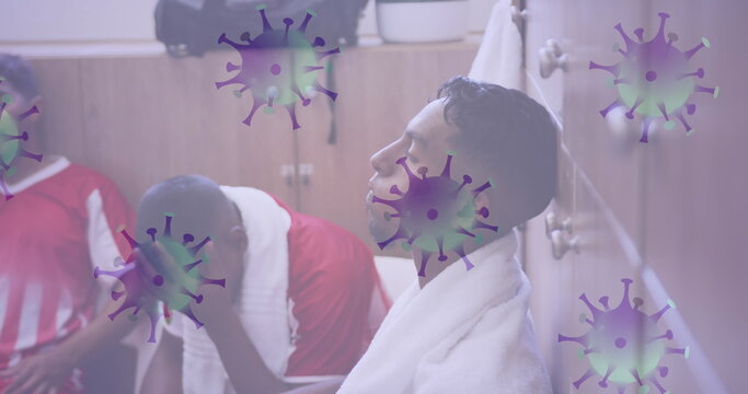 Image of covid 19 cells over disappointed football players in changing rooms
