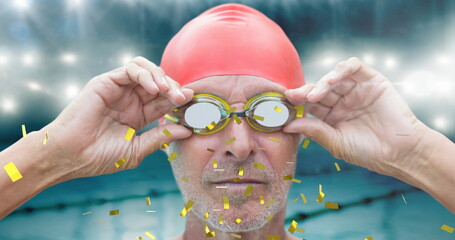 Golden confetti falling over senior male swimmer wearing swimming glasses against swimming pool
