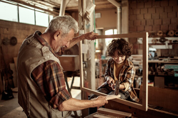 Fototapeta premium Grandfather teaching grandson woodworking in home workshop