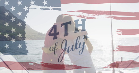 Image of text july 4th with american flag billowing over back view of couple embracing by sea