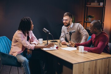 Radio hosts interviewing guest in soundproofed studio, engaging in dynamic conversation while...