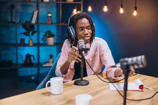 African American man content creator recording his audio podcast using professional microphone and headphones in a modern studio