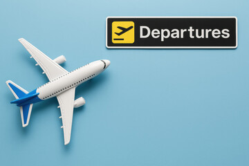 A model airplane next to a "Departures" sign on a blue copyspace background, symbolizing air travel and airport dynamics.