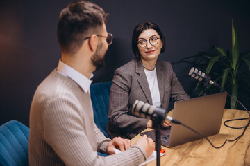 Two podcasters are recording an episode in a professional studio, engaging in conversation and...