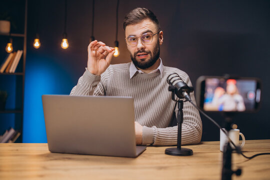Young man recording a podcast using a professional microphone and laptop in a home studio, gesturing while speaking