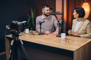 Professional podcasters collaborating, speaking into microphones while recording creative content in modern studio setting