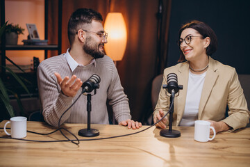 Two podcasters are recording an episode in a professional studio, engaging in conversation and...