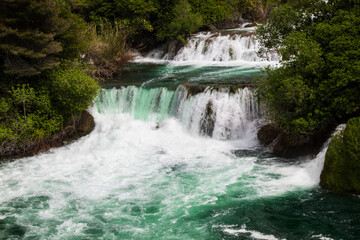 Obraz premium Scenic view of cascading waterfalls surrounded by lush green vegetation in a serene natural landscape