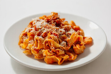 Fresh Italian tagliatelle with meat and tomato sauce, on white plate with light background. Traditional style, warm red tones, simple composition, isolated plate.