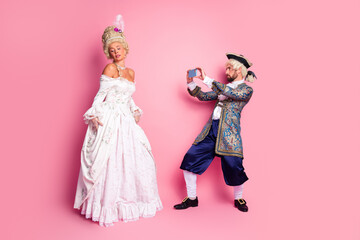 Elegant couple posing in historical costumes with a pink background, emphasizing nobility, royalty, and vintage charm at a themed carnival