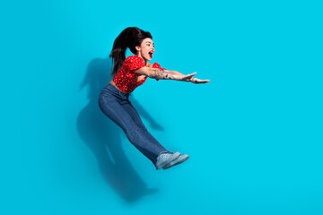 Young woman jumping with excitement against a blue background wearing casual attire, showcasing a...