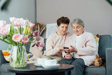 A young woman explaining her senior mother or grandma how to use smartphone. Retired lady discovering mobile technology for calling, texting, buying online, playing games, using medical apps.