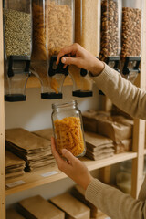 Main remplissant un bocal en verre de pâtes fusilli dans une épicerie vrac, contenant réutilisable et consommation zéro déchet