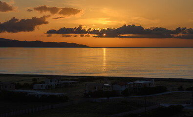 Fototapeta premium Golden sunset over tranquil waters and distant hills, casting reflections along the shoreline as day transitions to night