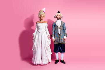 Fototapeta premium Elegant couple in vintage aristocratic costumes posing against a bright pink background for a themed carnival or royal masquerade party