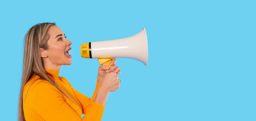 Young woman enthusiastically speaking into a megaphone against a bright blue background in a studio...