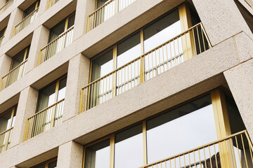 Fototapeta premium Modern building facade. Repetitive golden balconies. Abstract architectural lines. Urban lifestyle concept. Symmetrical window pattern. City apartment view. Exterior housing design.