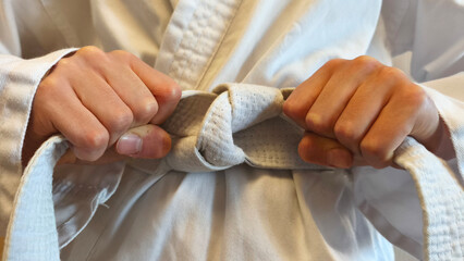 Close up Karate fighter dress up kimono and tightens or ties the white first belt before training