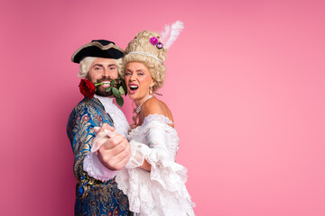 Elegant couple in vintage costumes dancing together in a romantic pose on a pink background